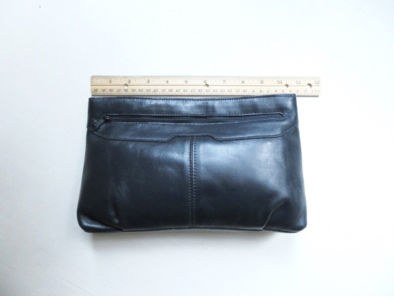 May include: A black leather clutch purse with a zippered pocket and a flap closure.