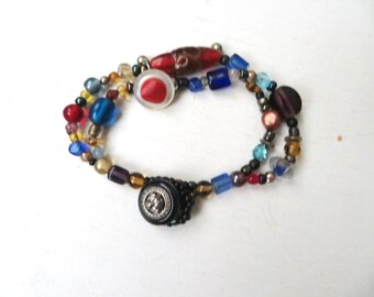 May include: A multi-strand bracelet with a variety of colorful beads, including red, blue, gold, and brown. The bracelet features two buttons, one red and one black with a silver design.