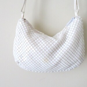May include: A white, chainmail-style shoulder bag with a silver chain strap.