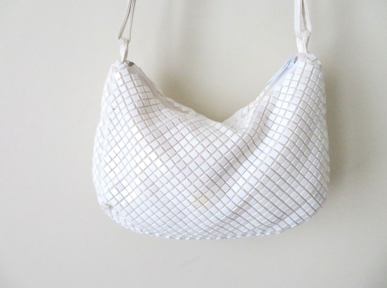 May include: A white, chainmail-style shoulder bag with a silver chain strap.