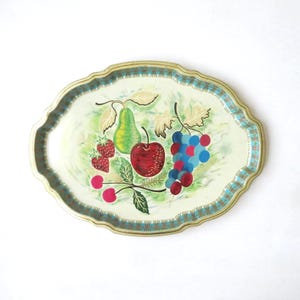 May include: Oval metal serving tray with a painted fruit design. The tray features a pear, apple, grapes, strawberries, and cherries. The tray has a scalloped edge with a teal and gold border.