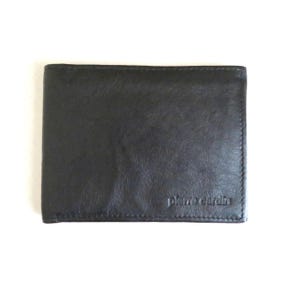 Puede incluir: Una cartera de cuero negro con el logotipo de Pierre Cardin en relieve en la esquina inferior derecha. La cartera es rectangular y parece estar doblada. El cuero tiene un aspecto ligeramente texturizado.