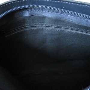 May include: The inside of a dark blue leather bag with a zipper closure. The lining is a dark fabric.