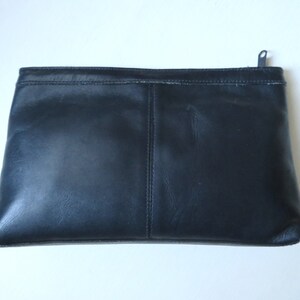 May include: A black leather clutch with a zipper closure. The clutch has a seam down the center and is made of a smooth, textured leather.