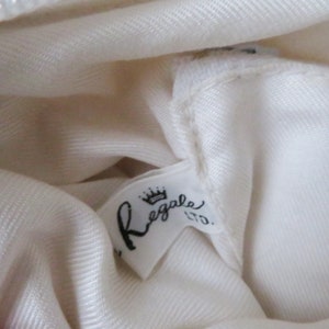 May include: White fabric with a white label that says "Regale Ltd." with a crown above the word "Regale".