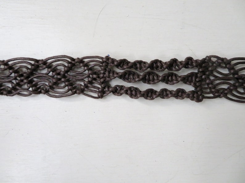 Puede incluir: Un cintur&oacute;n de macram&eacute; marr&oacute;n con un dise&ntilde;o tejido. El cintur&oacute;n presenta una serie de patrones anudados, creando un accesorio texturizado y decorativo. El cintur&oacute;n mide aproximadamente 5 cm de ancho.