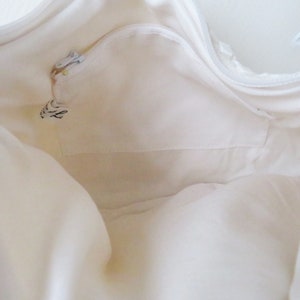 May include: White canvas tote bag with a zippered pocket on the inside. The bag is empty and the zipper is open.