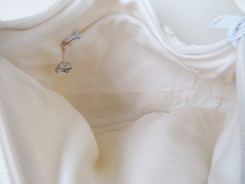 May include: White canvas tote bag with a zippered pocket on the inside. The bag is empty and the zipper is open.