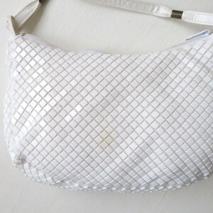 May include: A white chainmail shoulder bag with a white leather strap.