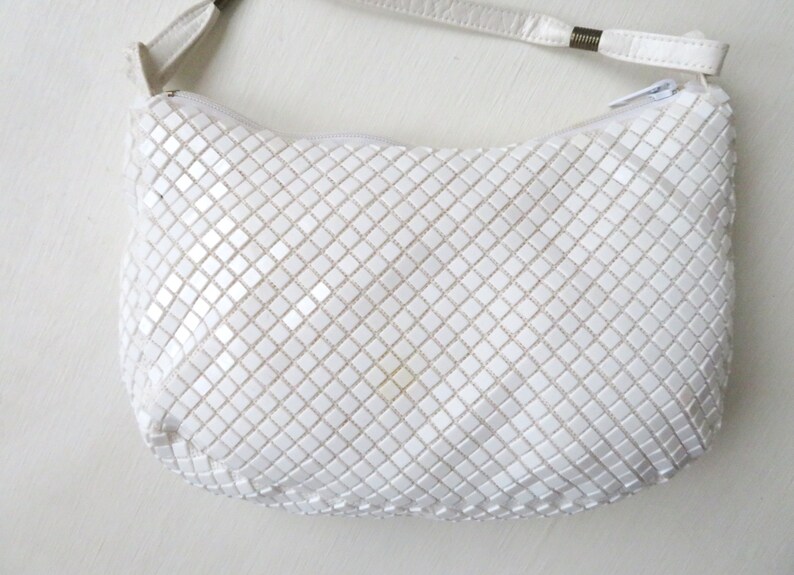 May include: A white chainmail shoulder bag with a white leather strap.