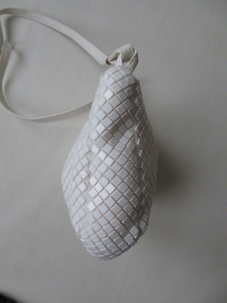 May include: A white, small, square-shaped handbag with a white strap. The bag is made of a textured material that resembles small squares.