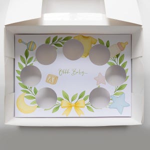 May include: A white box with a baby shower theme. The interior features a card with cut-out circles, surrounded by illustrations of baby items like a rattle, onesie, and bottle. The text "Ohhh Baby...." is also visible.