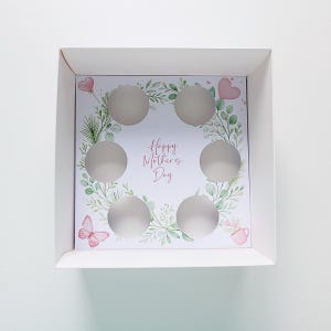 Puede incluir: Una taza de cerámica blanca con un asa negra y el texto "But First, Coffee" en un estilo manuscrito. La taza está sobre una superficie blanca. La taza mide aproximadamente 10 cm de alto.