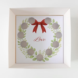 Puede incluir: Impresión enmarcada con un diseño de corona con un lazo rojo y la palabra "Love". La corona está compuesta por hojas verdes y círculos grises. El marco es de color beige claro.