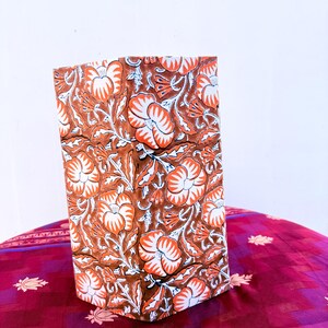 May include: A rectangular, fabric-covered box featuring a repeating floral pattern in shades of brown, orange, and white. The flowers and leaves are stylized, creating a vintage aesthetic. The box is placed on a patterned, reddish-purple fabric.