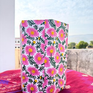 May include: A rectangular, floral-patterned container with a white background. The container is covered in pink flowers with yellow centers and green leaves. The container sits on a red patterned surface.