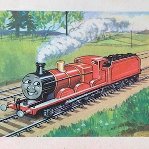 May include: A smiling red steam train with black accents and a coal car, traveling on tracks through a green field. White smoke billows from the smokestack. The background features trees and rolling hills.