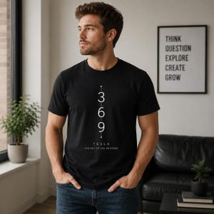 May include: A black short-sleeved t-shirt featuring a vertical white graphic with the numbers 3, 6, and 9 stacked in a column. Below the numbers, the text reads TESLA and THE KEY TO THE UNIVERSE in a clean, sans-serif font centered on the chest.