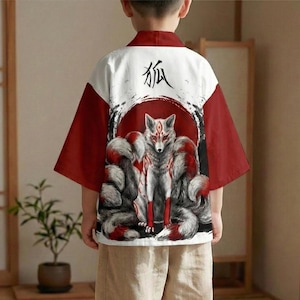 Può includere: Un top in stile kimono bianco e rosso con un'illustrazione di volpe sul retro. La volpe ha più code ed è ambientata su un cerchio rosso. Il carattere giapponese per volpe è stampato sopra l'illustrazione.
