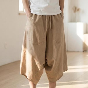 May include: Tan culottes with a drawstring waist and large front pockets. The loose-fitting, cropped pants are made of a lightweight fabric. The model is wearing a white t-shirt.