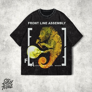 以下が含まれることがあります： 黒いTシャツ。黄色とオレンジ色の生き物が光る球体を持っているグラフィックデザイン。上部に「FRONT LINE ASSEMBLY」、グラフィックの下に「FLAVOUR of the weak」の文字。シャツは使い古されたような外観です。