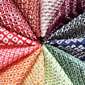 Op de afbeelding: Een cirkelvormige opstelling van stoffen stalen met een herhalend ruitpatroon. De kleuren variëren van rood tot oranje, geel, groen, blauw en paars. De stof heeft een getextureerde afwerking.
