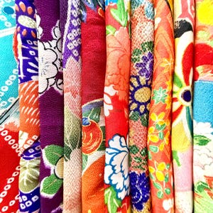 May include: A collection of folded fabric strips featuring vibrant, multi-colored patterns. The textiles display intricate floral motifs, geometric shapes, and traditional designs in shades of red, purple, orange, blue, yellow, and green.