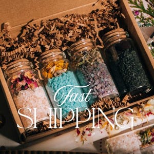 Puede incluir: Una caja de regalo que contiene cuatro frascos de vidrio llenos de sales de ba&ntilde;o y productos bot&aacute;nicos de colores. Los frascos tienen tapones de corcho y est&aacute;n dispuestos en una caja de cart&oacute;n con papel triturado. Los frascos contienen contenido rosa, azul, morado y verde.