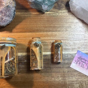Puede incluir: Tres frascos de vidrio de diferentes tama&ntilde;os, llenos de hierbas secas y sellados con tapas decorativas. Los frascos est&aacute;n adornados con cera y cuerda. Tambi&eacute;n hay una peque&ntilde;a tarjeta con el texto "Landing Your Dream Job SPELL JAR".