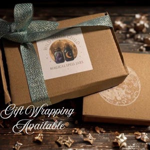 Puede incluir: Dos cajas de cart&oacute;n marr&oacute;n, una con una etiqueta que dice "Wild Moon Child Magical Spell Jars", est&aacute;n atadas con una cinta verde azulado. El texto "Gift Wrapping Available" est&aacute; escrito en cursiva en la parte inferior.