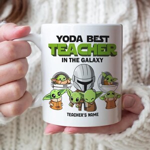 May include: White ceramic mug featuring the text "YODA BEST TEACHER IN THE GALAXY" in green and black. The mug also displays illustrations of Baby Yoda and a Mandalorian helmet. The words "TEACHER'S NAME" are at the bottom.