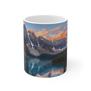 May include: White ceramic mug featuring a scenic landscape of mountains, a lake, and a sunset. The mountains are snow-capped, and the lake reflects the sky. The mug is cylindrical and has a glossy finish.