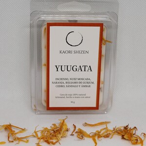 Puede incluir: Un ambientador de cera rectangular en un envase de plástico transparente. La etiqueta dice "KAORI SHIZEN YUUGATA" con una lista de ingredientes. Pétalos de naranja secos esparcidos. El producto pesa 90g.