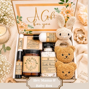 May include: A gift box containing a crochet bunny rattle, two bear-shaped washcloths, a vanilla body oil roll-on, a bar of oatmeal milk honey goat's milk soap, a jar of Hey Mama soy candle, a bottle of lotion, and a jar of herbal sitz bath soak.