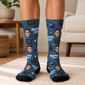 May include: Blue crew socks featuring a repeating pattern of a person's face, the text "Missionary Dad," black rectangular name tags reading "Elder Davis," small white stars, and the New Zealand flag printed across the fabric with black toes.
