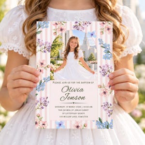 May include: A baptism invitation card featuring a pink and white striped background with watercolor floral accents. The center displays a photo of a girl in a white dress. Text reads: Please join us for the baptism of Olivia Jenson, March 15 2026.
