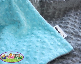 May include: A soft, blue and gray baby blanket with a textured, dotted pattern. The blanket has a tag that says "Lil' Cub Hub".