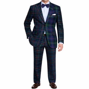 Puede incluir: Un traje a cuadros azul marino con detalles en verde, rojo y amarillo. El traje incluye una americana con pañuelo de bolsillo, pantalones a juego, una camisa blanca y una pajarita azul. El modelo lleva zapatos de cuero marrones.