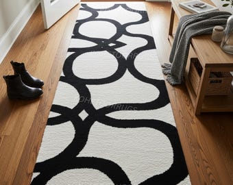 May include: A long, rectangular rug with a repeating black and white geometric pattern. The rug is placed in a hallway with wooden flooring. The design features large, interconnected black shapes against a white background.