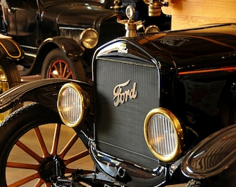 May include: A black 1920s Ford Model T car with a chrome grill and headlights. The car has a wooden dashboard and a black leather interior. The car is in excellent condition and has been restored to its original glory.