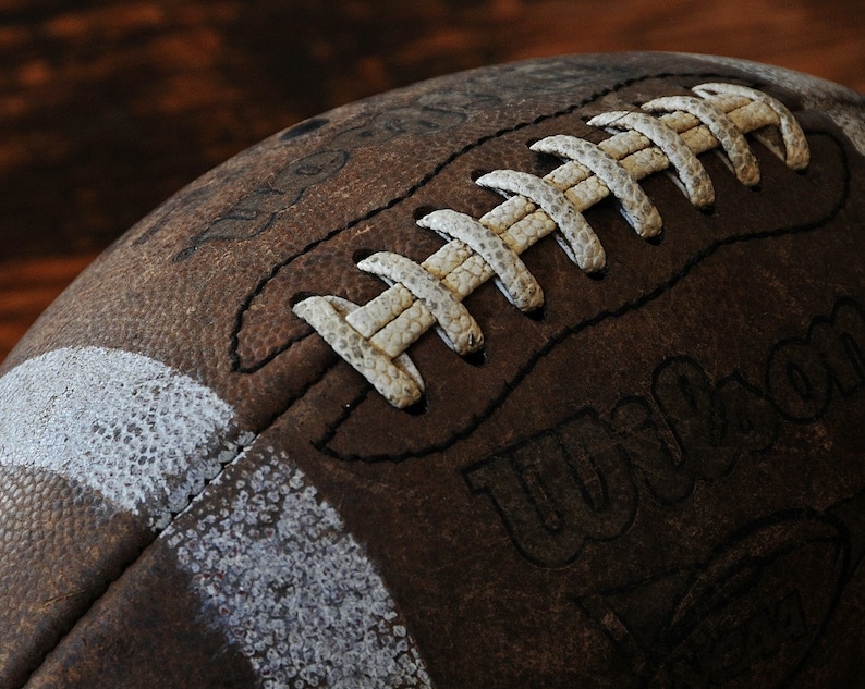 May include: Close-up of a brown leather football with white laces and a white stripe. The football has the word "Wilson" printed on it.