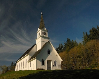 May include: A white church with a tall steeple and a pointed roof. The church is surrounded by trees and a grassy lawn. The sky is blue with white clouds.