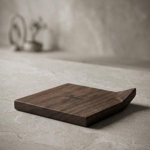 Puede incluir: Una bandeja de madera marrón oscuro con un borde curvo. La bandeja tiene forma cuadrada y la palabra "James" está grabada en la superficie. La bandeja está sobre una superficie gris claro.