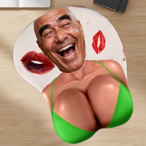 May include: Ergonomic mousepad featuring a smiling man's face, a green bikini top, and red lipstick kiss marks. The mousepad is designed with a wrist rest for comfort and support during computer use.