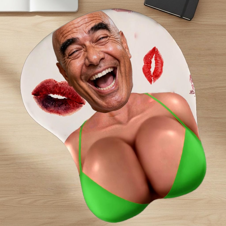 May include: Ergonomic mousepad featuring a smiling man's face, a green bikini top, and red lipstick kiss marks. The mousepad is designed with a wrist rest for comfort and support during computer use.