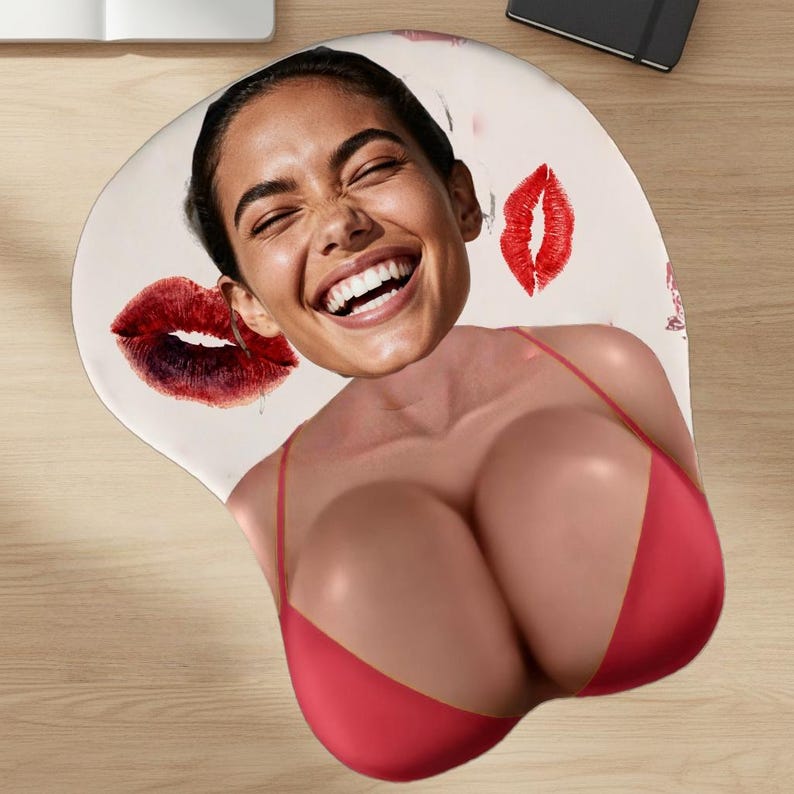 May include: Ergonomic mousepad featuring a smiling woman's face and red lips. The mousepad has a red bikini top design, providing wrist support. The background is a light beige color.