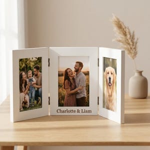 Może przedstawiać: Biała, trzypanelowa ramka na zdjęcia z trzema różnymi zdjęciami. Środkowy panel ma u dołu napis "Charlotte & Liam". Ramka stoi na drewnianej powierzchni.