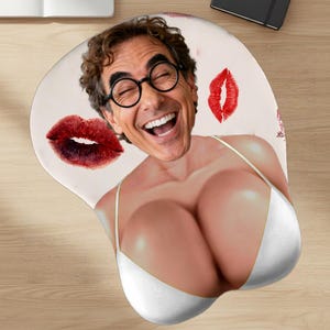 May include: Ergonomic mousepad featuring a smiling man's face with round glasses, superimposed on a woman's body wearing a white bikini top. Red lipstick kiss marks are scattered across the light pink surface.
