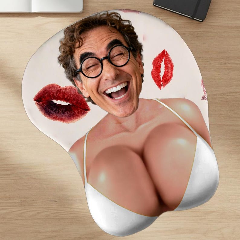 May include: Ergonomic mousepad featuring a smiling man's face with round glasses, superimposed on a woman's body wearing a white bikini top. Red lipstick kiss marks are scattered across the light pink surface.