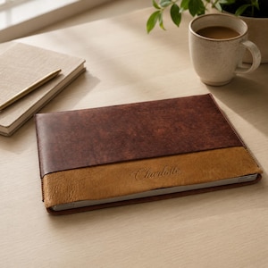 Könnte beinhalten: Eine rechteckige Laptoptasche mit zweifarbigem Design, bestehend aus einem dunkelbraunen oberen Teil und einem helleren beigen unteren Teil. Der beige Bereich ist mit dem Namen Charlotte in einer kursiven Schriftart geprägt.